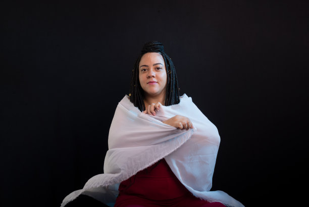 照片中的美女扎着辫子，穿着白布包裹的红色衣服。黑色背景的工作室肖像。图片下载