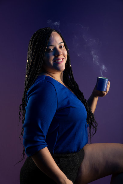 一个穿着蓝衣服，扎着辫子的漂亮女人的画像，手里拿着一杯冒着烟的咖啡。孤立的深蓝色背景。图片下载