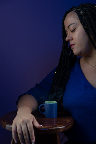 一个美丽的女人的肖像，她的头发上扎着辫子，穿着蓝色的衣服，看着一杯咖啡。孤立的深蓝色背景。图片下载