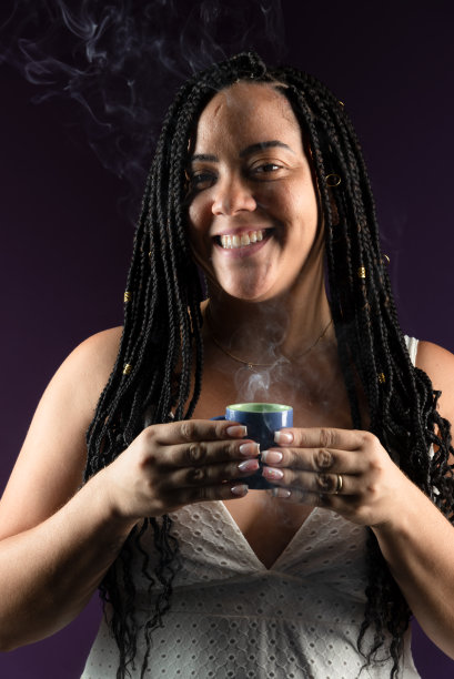 梳着辫子的美女端着一杯热气腾腾的咖啡。穿着白色的衣服。孤立在深紫丁香背景上。图片下载