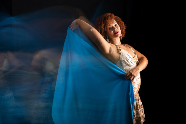 这张照片是以低速拍摄的，一个美丽的女人，她有着卷曲的红头发，正在用一块蓝色的布做动作图片下载