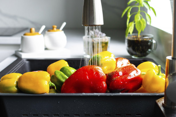 黄椒和红椒在专门的蔬菜托盘里洗净。水流倾泻在水槽里的辣椒上。现代厨房的内部图片下载