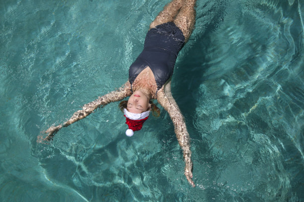 戴着圣诞帽的年轻女子在游泳池里放松。圣诞热带度假概念。图片下载