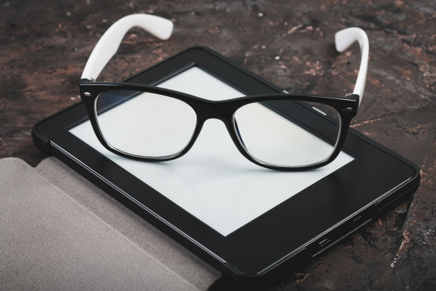 桌上有电子书和纸质书，还有一杯咖啡，一台笔记本电脑和老花镜。自我教育的概念。图片下载