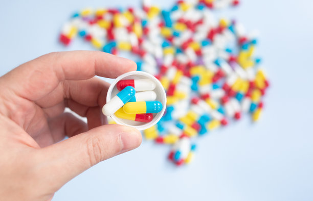 年轻人拿着一瓶药和不同的药片，浅蓝色的背景，设计的空间。图片下载