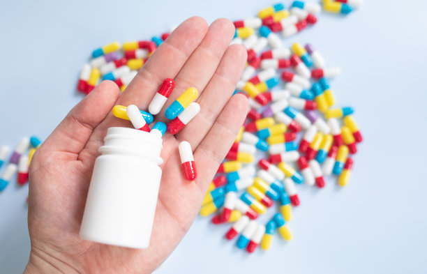 年轻人拿着一瓶药和不同的药片，浅蓝色的背景，设计的空间。图片下载