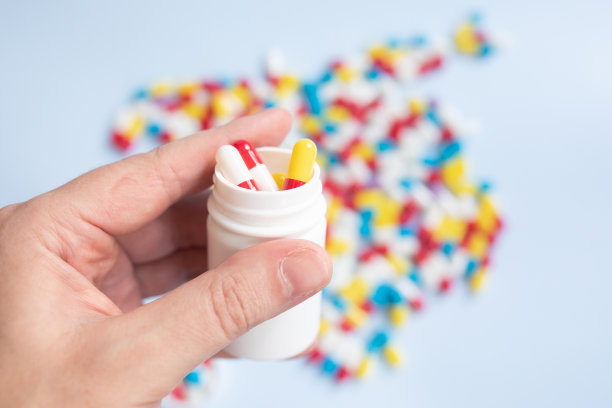 年轻人拿着一瓶药和不同的药片，浅蓝色的背景，设计的空间。图片下载