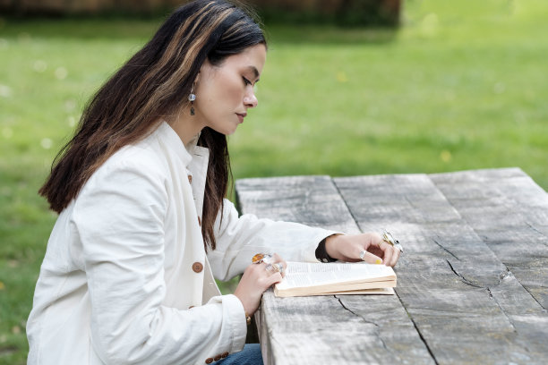 放松的女人在公园的桌子上看书。图片下载