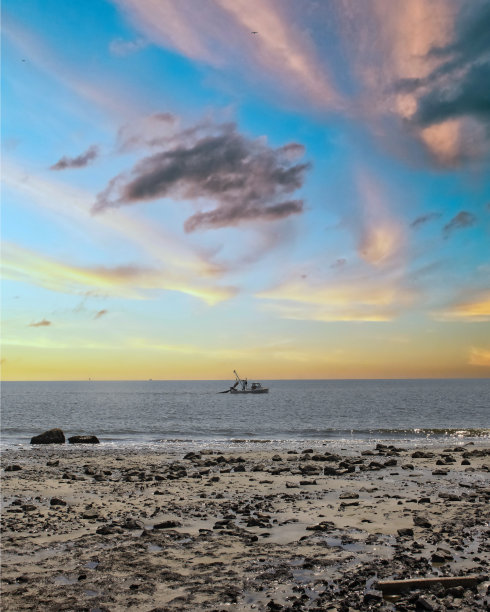 渔船或捕虾船在日落时分拖着网经过海滩图片下载