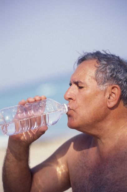 一位老人在海滩上用瓶子喝水图片下载