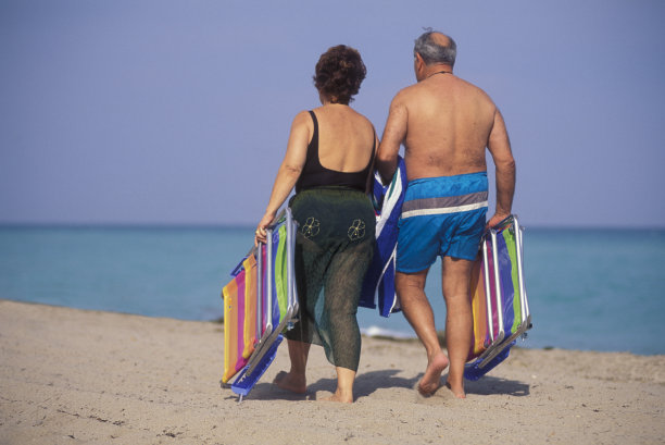 一对老年夫妇带着沙滩椅和毛巾在沙滩上散步图片下载