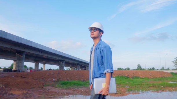 亚洲土木工程师拿着笔记本电脑，走在工地检查建设工程的道路高速公路。图片下载