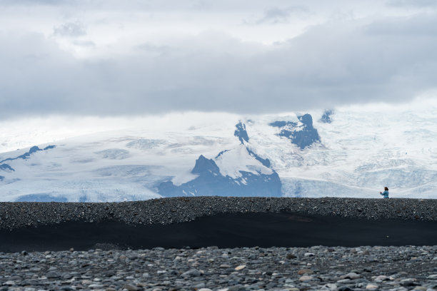 一名女游客在冰岛钻石海滩附近拍摄风景。背景中的大山显示了规模图片下载