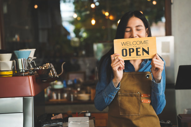 开放。咖啡师、女服务员穿着围裙，在现代咖啡馆、咖啡馆餐厅、零售店、小企业主、食品和饮料概念中打开标牌欢迎顾客。小生意，家庭老板。图片下载