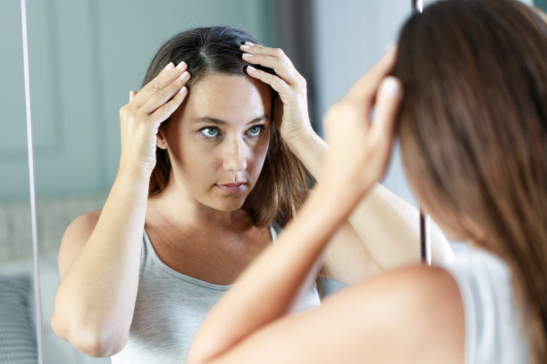 年轻女子照镜子，有脱发的问题图片下载