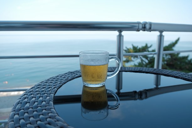 淡啤酒。冰镇的淡啤酒装在满是水珠的玻璃杯里。桌子上放着一杯啤酒，背景是平静的蓝色大海图片下载