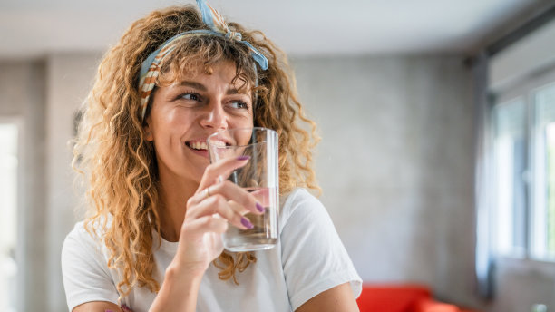 一个成年白人妇女坐在家里，端着一杯水开心地笑着图片下载