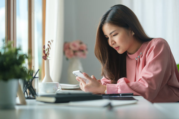 年轻女子坐在明亮的办公室里，用智能手机上网银行或在社交网络上交流。图片下载
