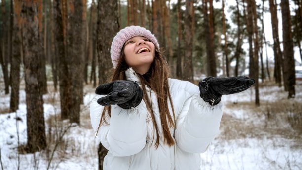 在冬天的森林里，一个快乐的、笑着的少女用手套捧着飘落的雪花图片下载