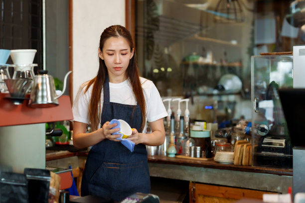 美丽的亚洲女孩在咖啡厅吧台后面擦咖啡杯。并且每天早上准备开咖啡店，随时准备接待顾客，咖啡店老板家庭小生意图片下载