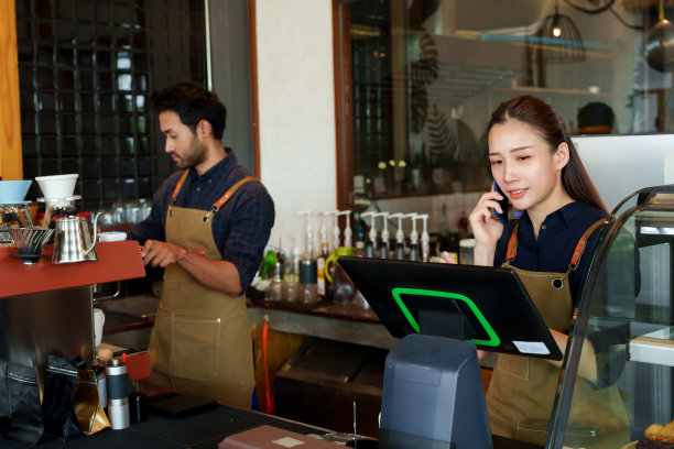 咖啡师夫妇拥有一家小型商业咖啡店。一名亚洲女子站在那里接老顾客的电话订单，一名男子在吧台后面准备煮顾客点的咖啡图片下载