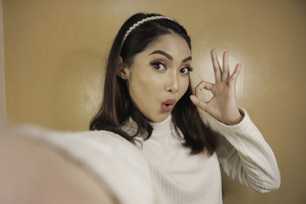 年轻的亚洲女子惊讶地用她的手机自拍。橙色背景的印尼女子。图片下载