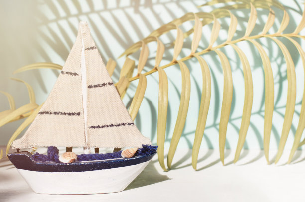 小型微型玩具帆船，热带棕榈叶以阴影为背景，阳光柔和柔和的淡色调。图片下载