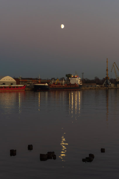 货船晚上在港口停泊。月亮在天空中照耀。图片下载