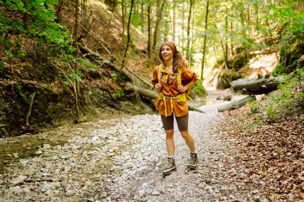 一个背着黄色背包的女旅行者正沿着一条徒步小径穿过山间的丛林。图片下载