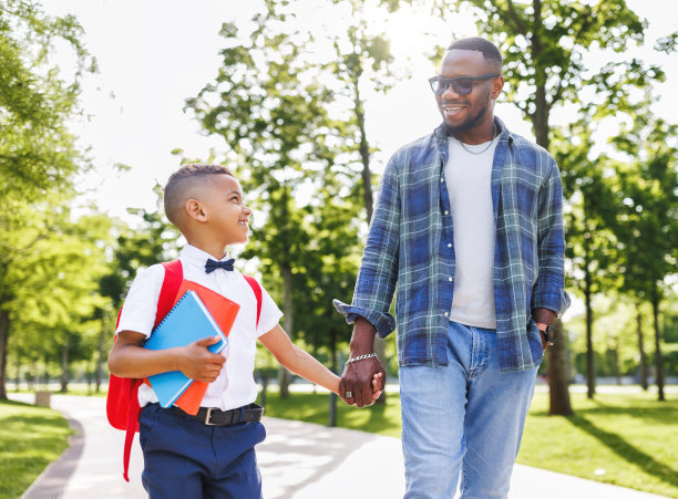 一个秋高气爽的日子，一个男生和爸爸一起去上小学一年级，他微笑着看着爸爸图片下载