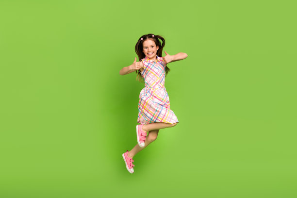 迷人、开朗、满意的女孩穿着时尚的裙子，在绿色背景上竖起大拇指图片下载