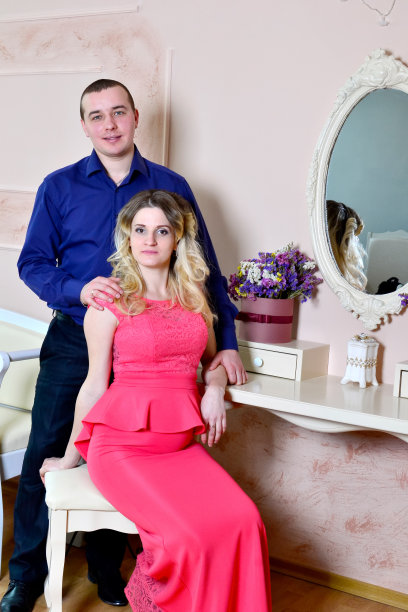 一对迷人的年轻夫妇正在家里庆祝节日。在镜子的背景上站着或坐着。丈夫拥抱怀孕的妻子。一家人站在一张有镜子的桌子旁坐着。高质量照片图片下载