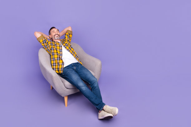 困倦有趣的照片积极的大胡子男人把胳膊放在脑后享受舒适的家具，空旷的空间孤立在紫色的背景图片下载