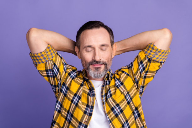 在紫色的背景上，平静的男人穿着格子格的衣服，双手抱在脑后，享受孤独的舒适图片下载