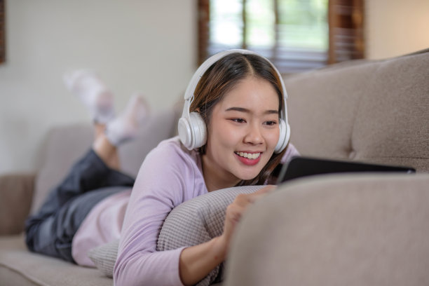 快乐的年轻女子坐在柔软的沙发上使用笔记本电脑。女士正在使用笔记本电脑。女学生正在用笔记本电脑键盘输入信息。图片下载