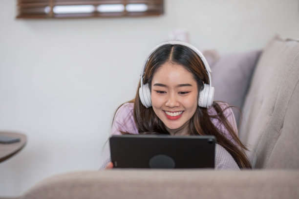 快乐的年轻女子坐在柔软的沙发上使用笔记本电脑。女士正在使用笔记本电脑。女学生正在用笔记本电脑键盘输入信息。图片下载