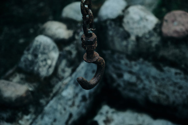 一个生锈的旧钩子挂在一个石头井上，周围是彩色玻璃窗和绿色植物图片下载