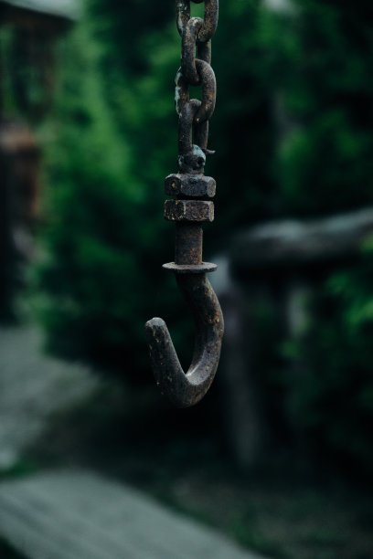 一个生锈的旧钩子挂在一个石头井上，周围是彩色玻璃窗和绿色植物图片下载