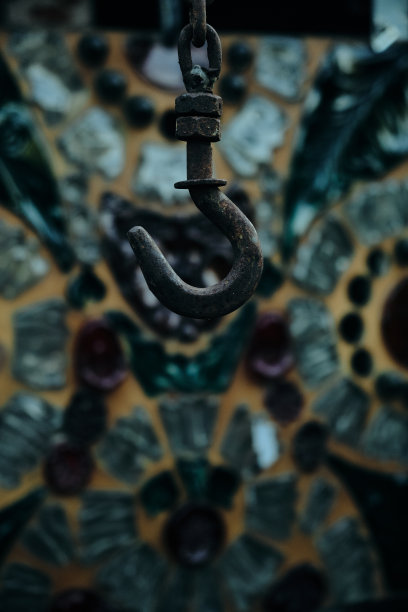 一个生锈的旧钩子挂在一个石头井上，周围是彩色玻璃窗和绿色植物图片下载