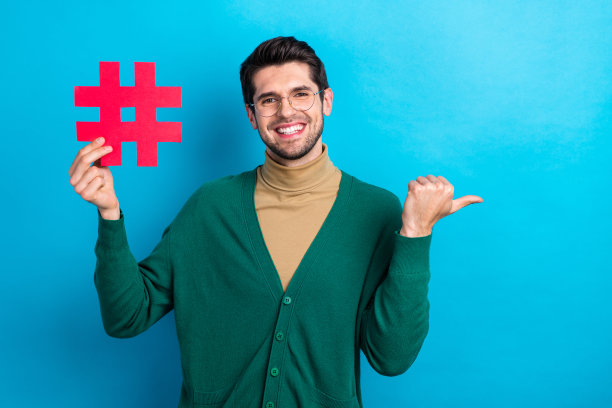 照片中年轻优雅的男子手持粉红色的纸别针标签符号直接手指空白的空间点击订阅孤立的蓝色背景图片下载