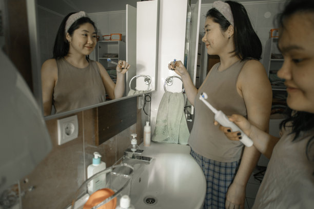 两个亚洲女孩坐在浴缸边上，把牙膏涂在牙刷上，开心地笑着图片下载