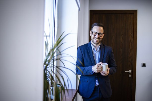 成功的经理或导演站在办公室里，喝着咖啡，看着镜头。图片下载