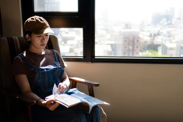 一位中国妇女正在窗边享受阳光和看书。图片下载