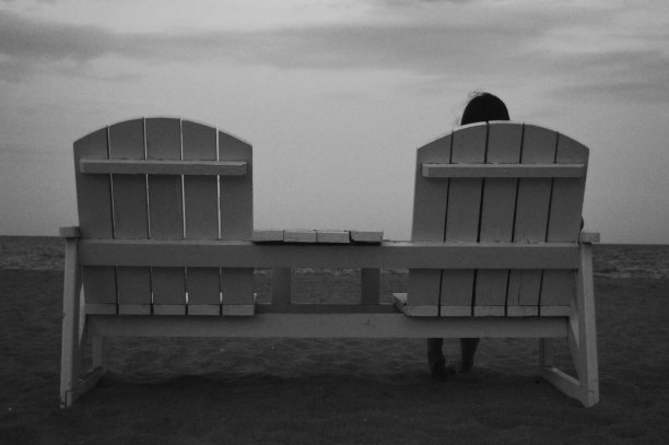 一个女孩正坐在沙滩上的木凳上，面朝大海，黑白照片图片下载