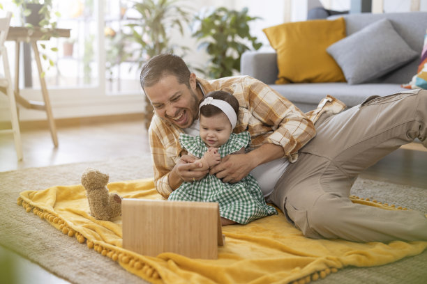 一位拉丁裔父亲躺在客厅的地板上和他的孩子玩耍，而他们则看着他平板电脑上的图画图片下载