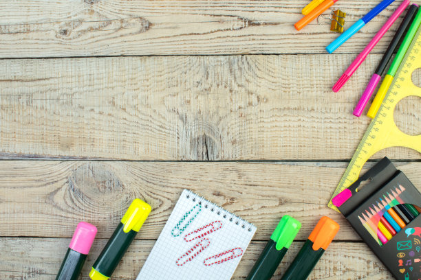 回到学校。剪刀，铅笔，回形针，记事本，记号笔，尺子。木桌上放着学习用品。带复制空间的俯视图。图片下载