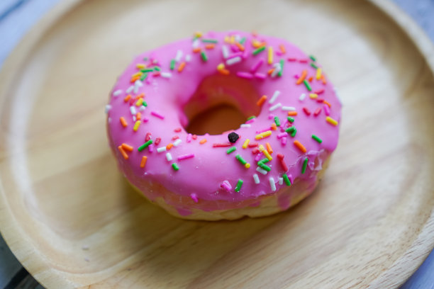 一个侧面的照片显示了一个木制盘子上有彩色糖霜的自制草莓甜甜圈。图片下载