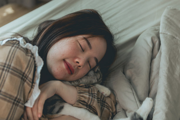 可爱的姜黄色猫躺在女人的手上。毛茸茸的宠物舒服地躺下来睡觉或玩耍。可爱舒适的背景与地方文字。早上在家就寝。图片下载