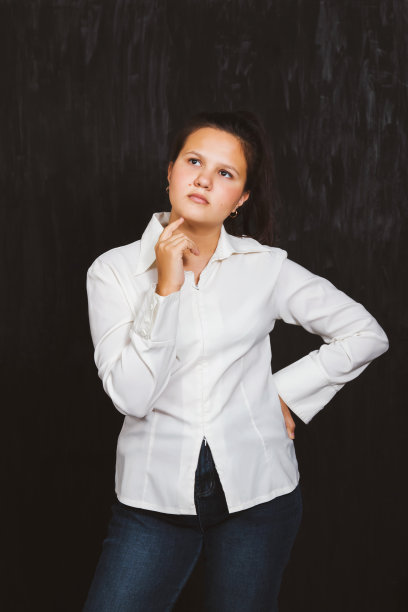一个女学生站在那里，黑色背景上穿着白衬衫，神情若有所思图片下载