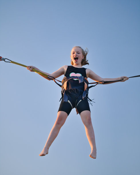 在游乐园和旋转木马上，小女孩用保险橡皮筋在蹦床上蹦蹦跳跳。图片下载
